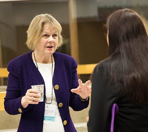 Dr. Barbara Kenner in a purple sweater and white shirt holding a cup and talking to a woman with long dark hair